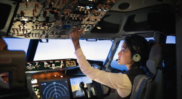 Rear view of a female pilot adjusting switches on the control panel while sitting inside cockpit. Woman operating the switches while flying an airplane.